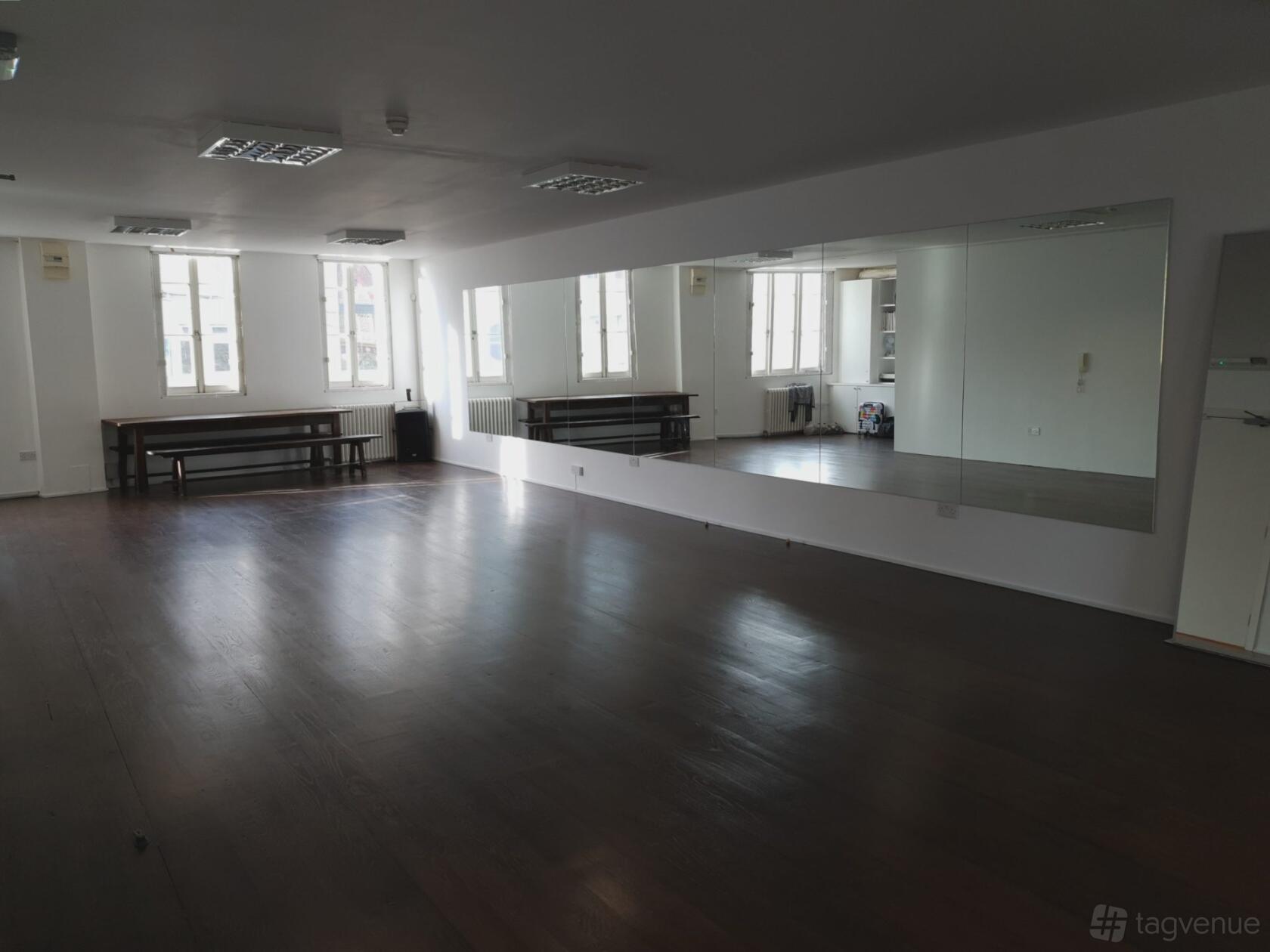 A rehearsal room with dark wood floors, large wall mirrors, and natural light from tall windows at Associated Studios.