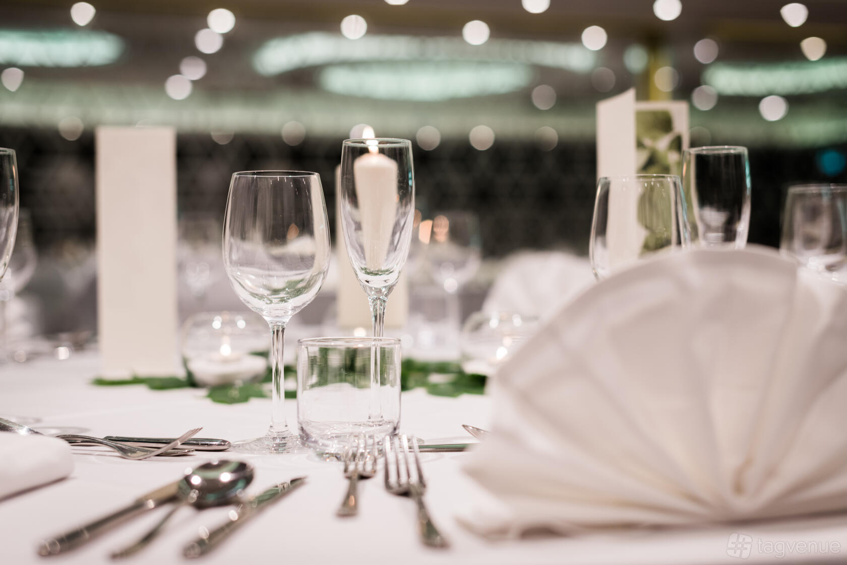 A hotel event space with elegantly set round tables, folded napkins, glassware, and a candle centerpiece at The Place Hotel.