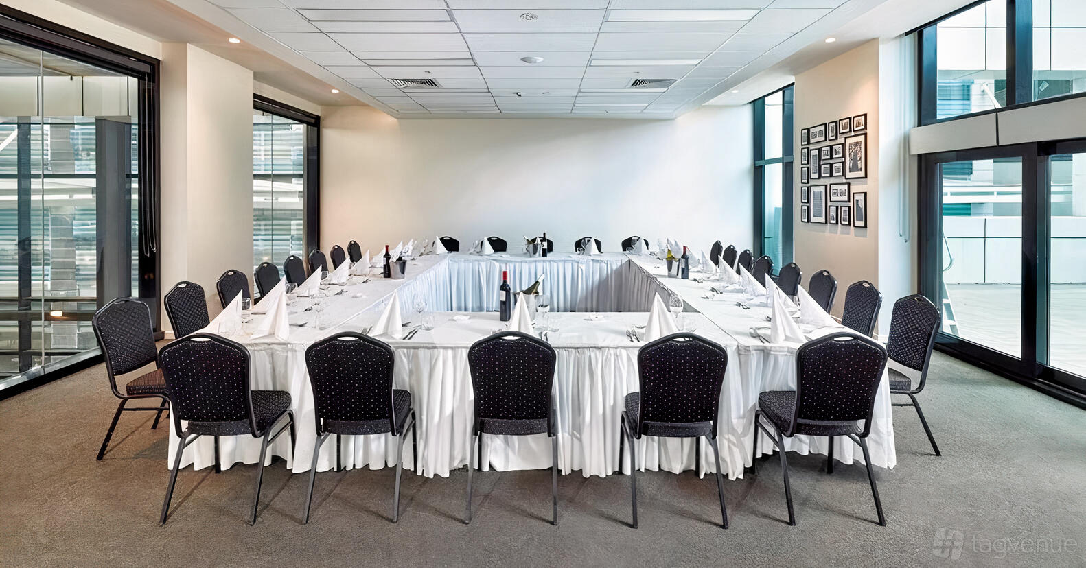 A meeting room with U-shaped tables draped in white linens, dark chairs, and framed photos at Pegasus Apart Hotel.