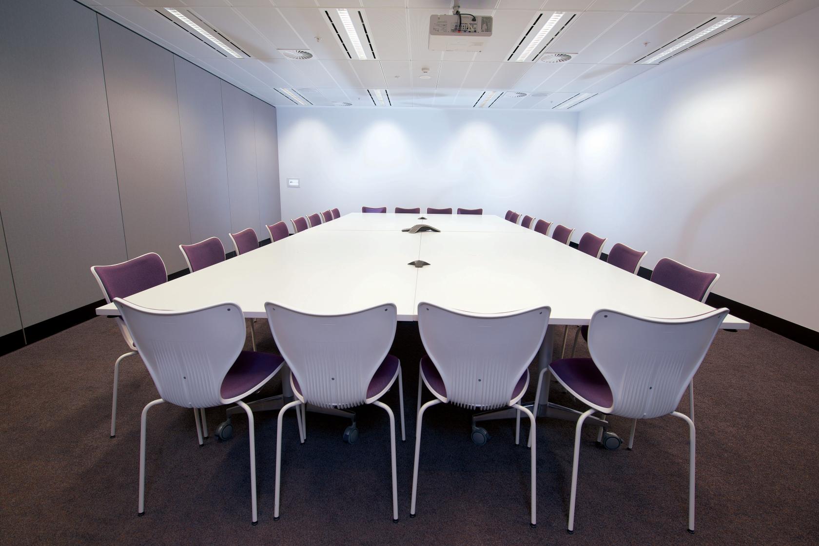 A meeting room with a large U-shaped table, ergonomic white chairs, and ceiling-mounted projector at Flex by ISPT at 4 National Circuit.