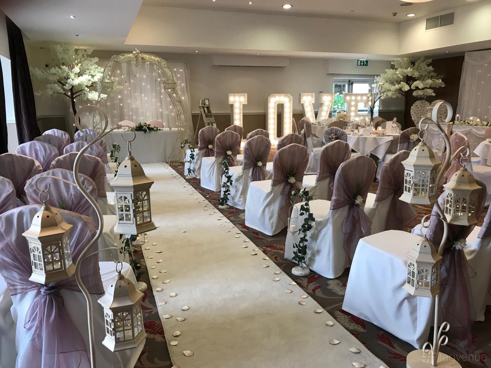 An event space with lantern-lined aisle, chair covers with sashes, and large illuminated letters at Hellaby Hall Hotel.