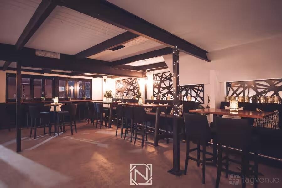 An event space in a bar with candlelit high tables, dark wood beams, and decorative wall panels at Niche Bar.