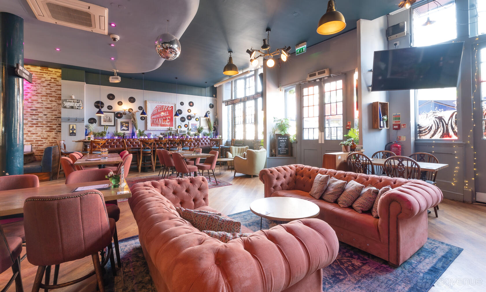 A bar in a pub with velvet tufted sofas, wood floors, and vinyl records wall decor at The Lighthouse.