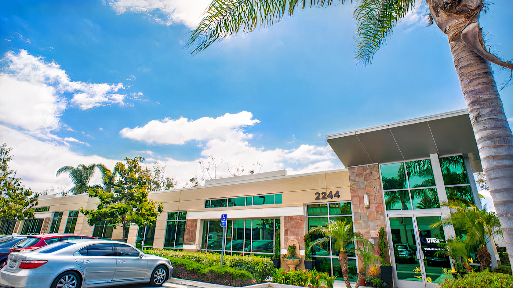 A conference centre with large glass windows, palm trees, and parking spaces at Prime Executive Offices.