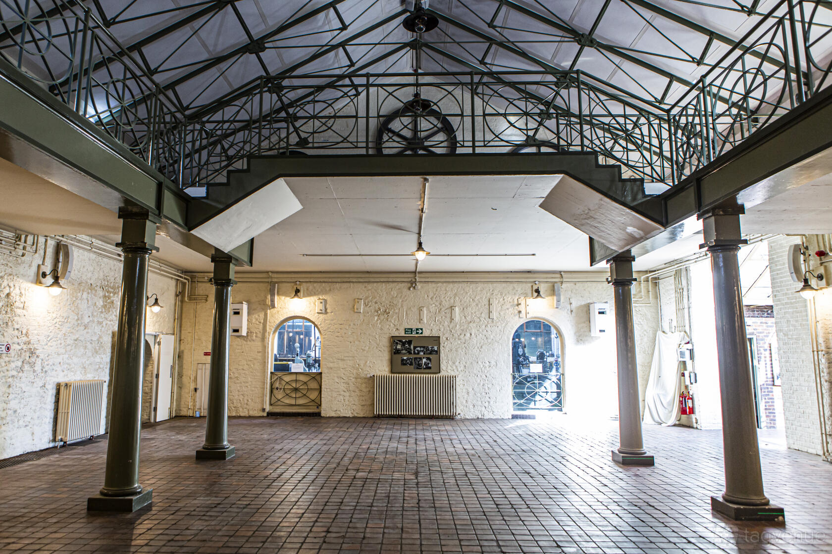 A historic hall with exposed brick walls, arched windows, tile flooring, and iron columns at The British Engineerium.