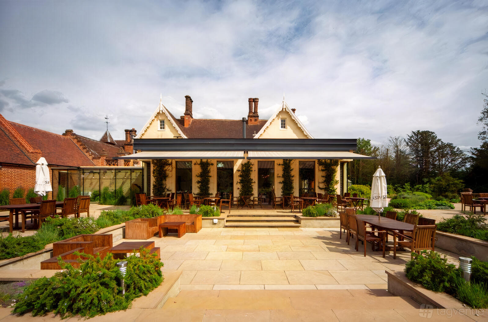 An outdoor event venue with wooden tables, chairs, and landscaped gardens in front of The Oaksmere.