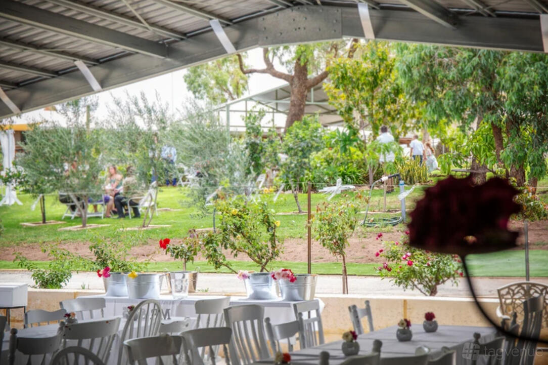 A barn with white chairs and tables overlooking a garden lawn and mature trees at Rose Social Baldivis.