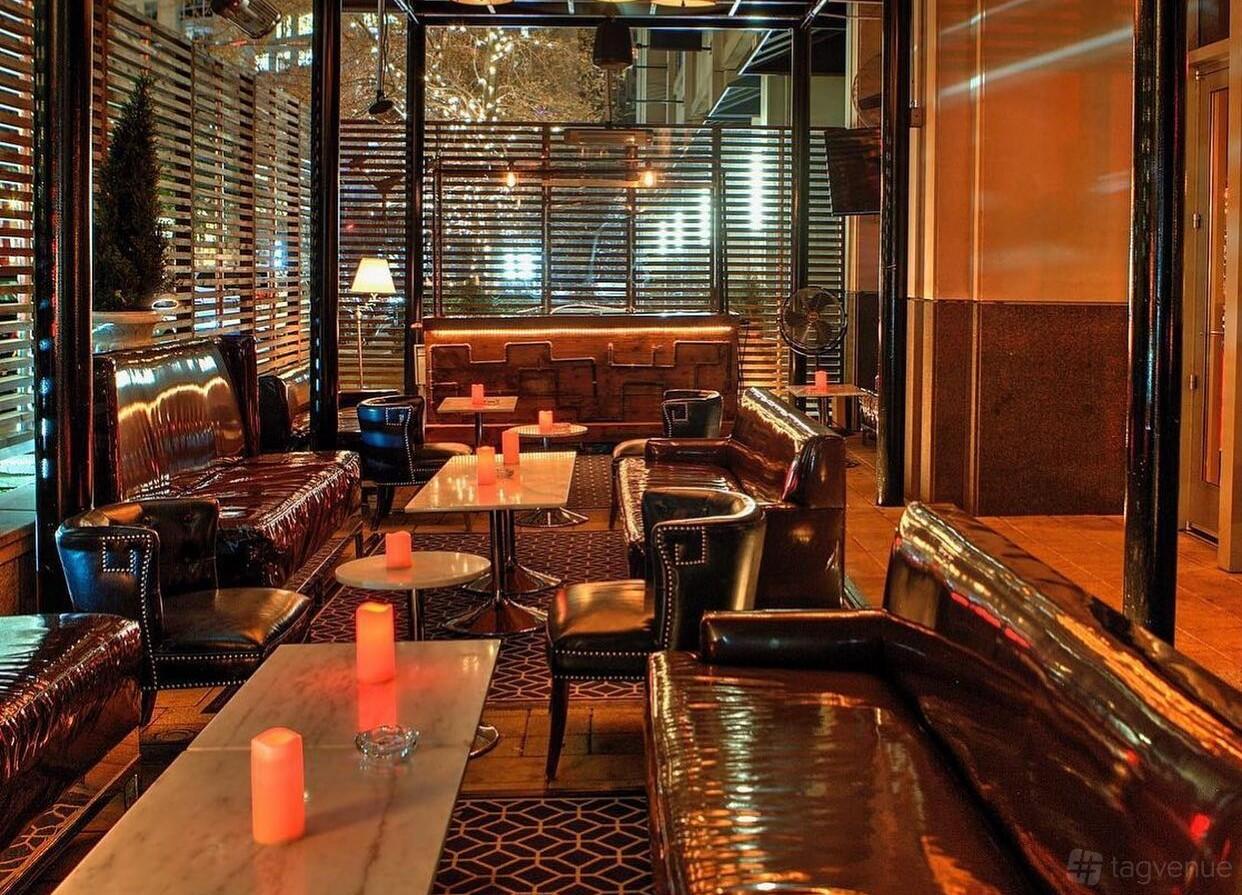 A lounge with leather sofas, marble tables, and candlelight ambience at The Tipsy Alchemist.