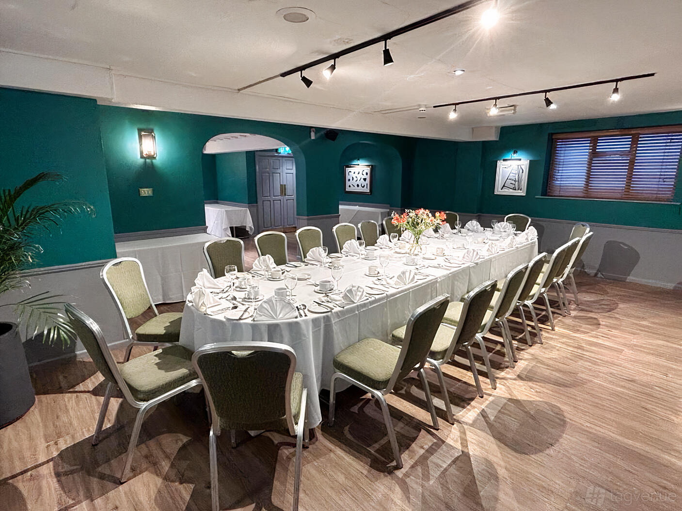 An event space with a U-shaped table set with white linens and green chairs at The Great Barr Hotel.
