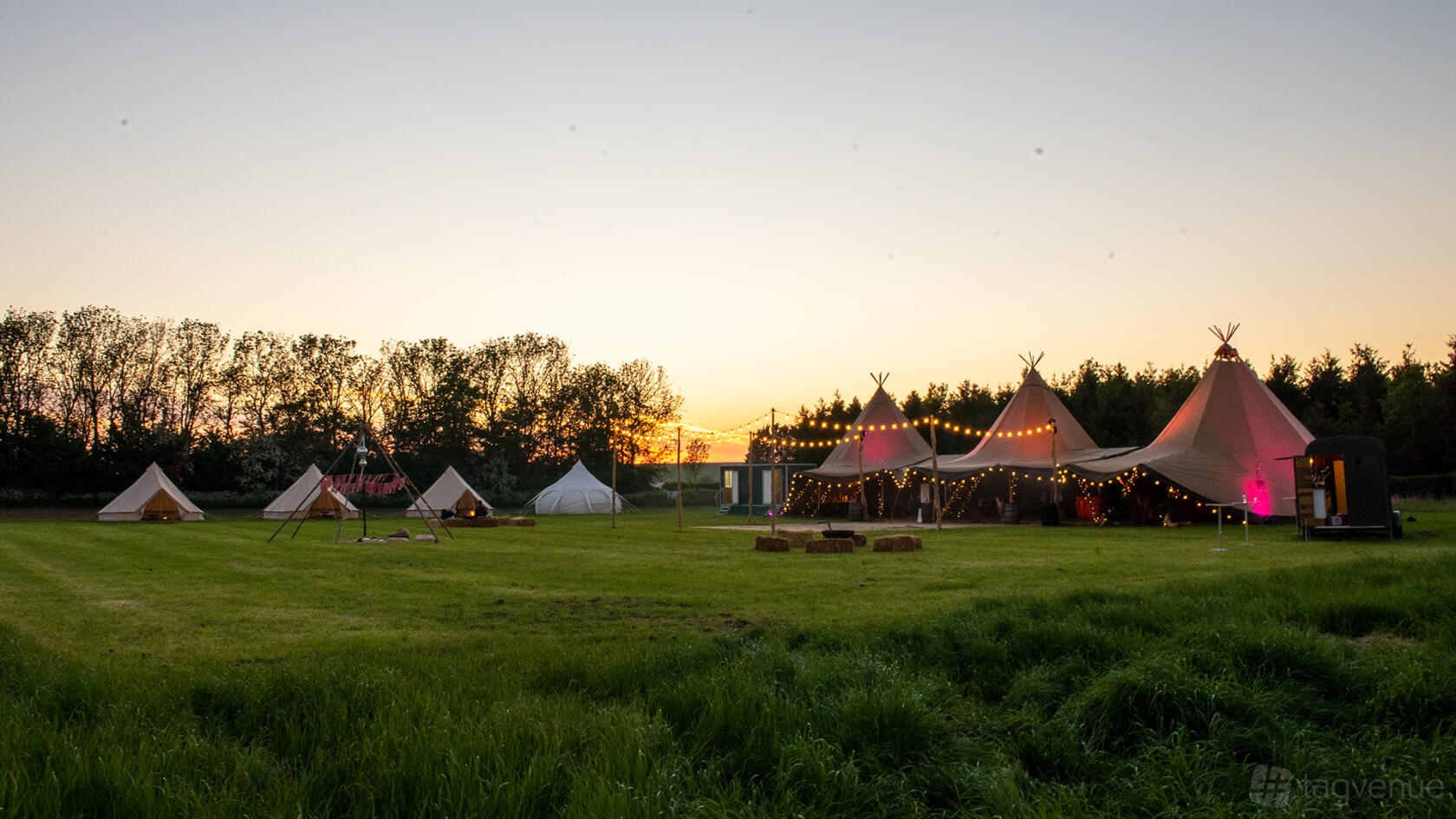 An open air venue with large tipis, string lights, and grassy fields at Bygrave Woods.
