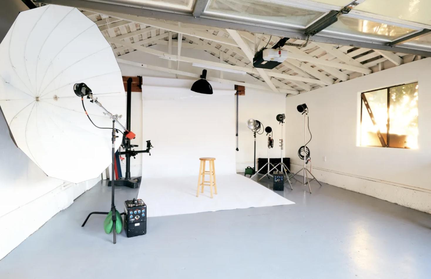 A photo and film studio with white cyclorama backdrop, studio lighting, and wooden stool at Fifth District Studio.