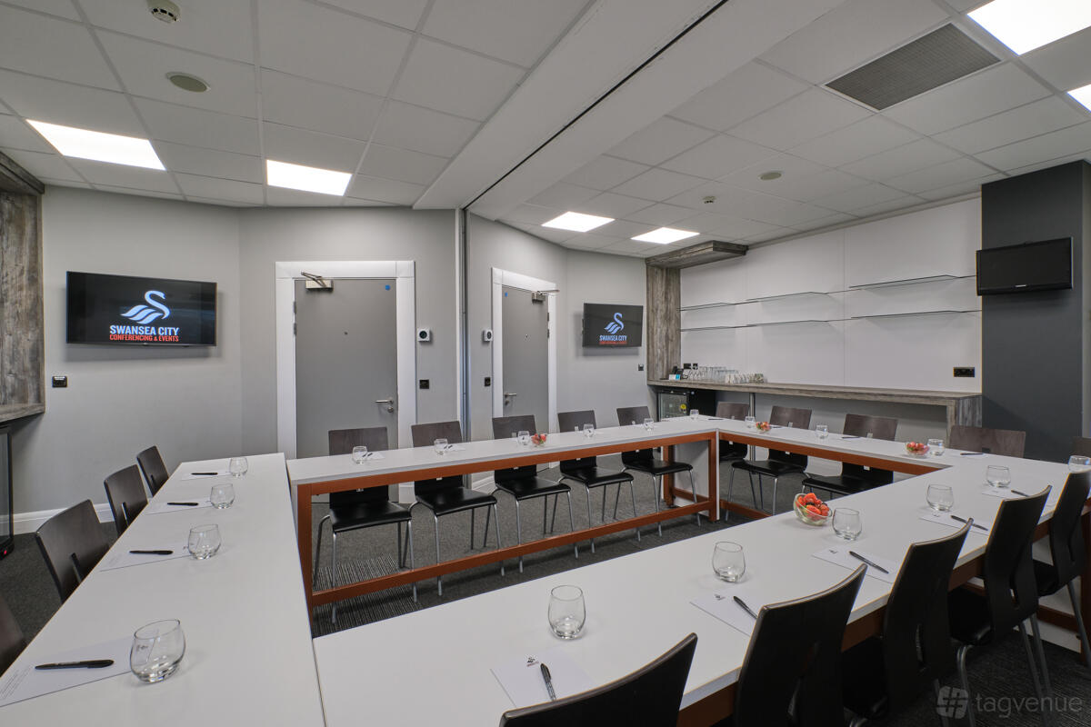 A meeting room with U-shaped tables, black chairs, wall-mounted screens, and notepads in Swansea.com Stadium Executive Suites.