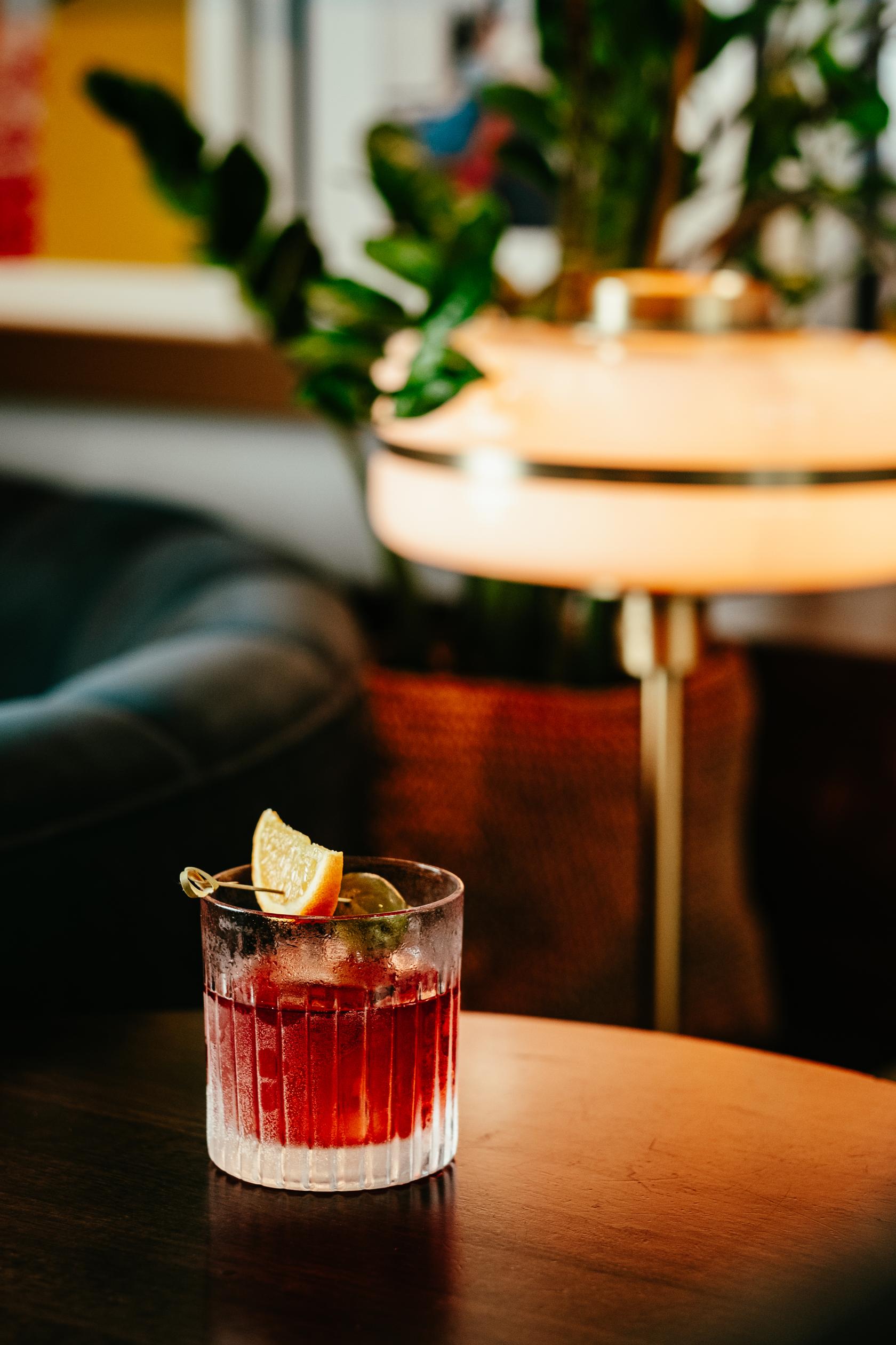 A cocktail bar event space with a leather sofa, warm lamp lighting, and a drink garnished with citrus at LOCKES Bar Covent Garden.