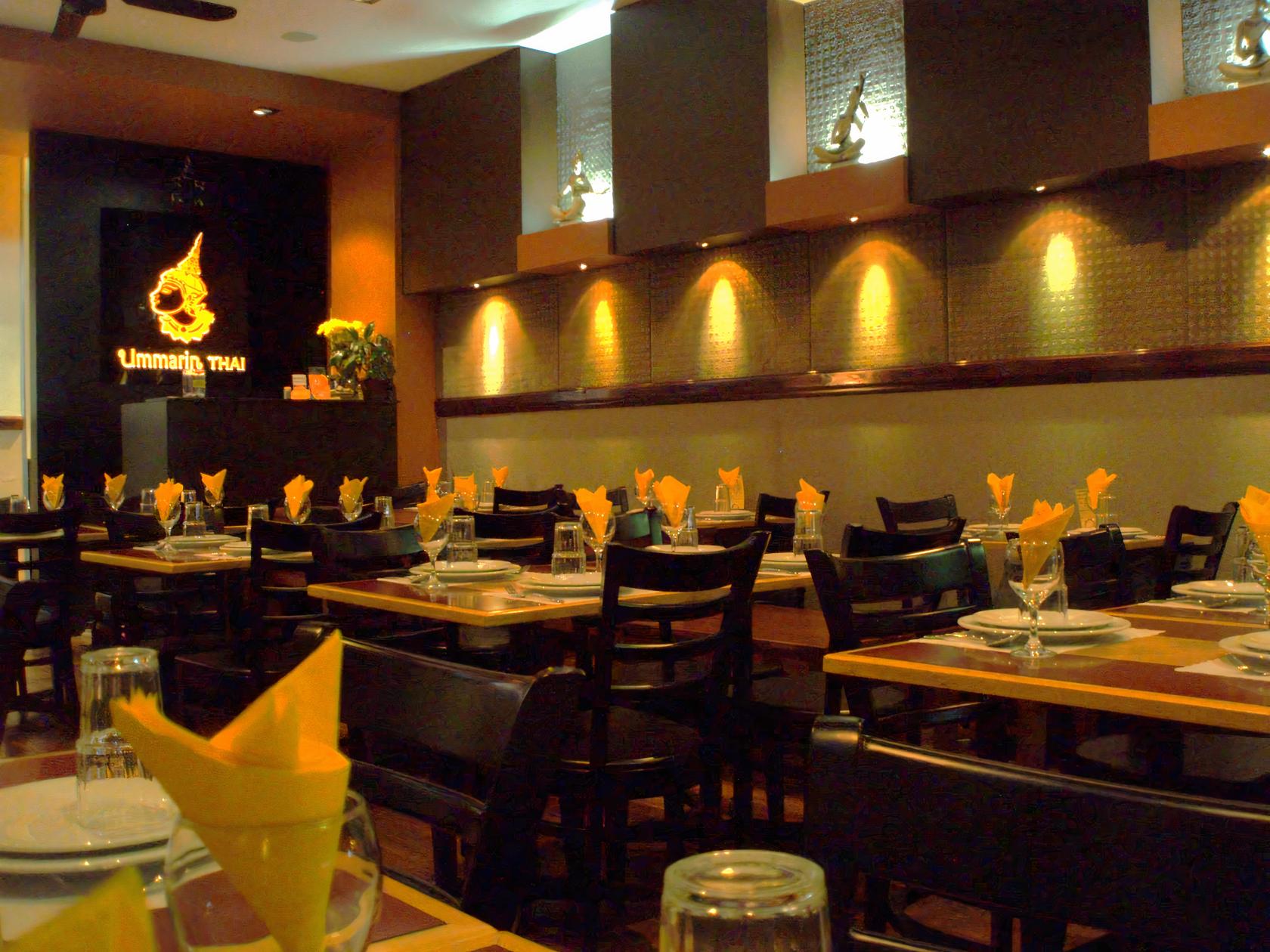 An event space in a restaurant with wooden tables, black chairs, and yellow napkins at Ummarin Thai Restaurant.