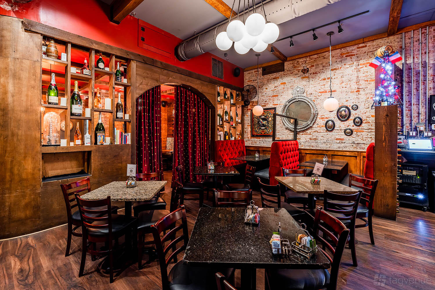 A restaurant with exposed brick walls, red velvet booths, and globe pendant lighting at Chez Fabien - Grapevine French Cuisine.
