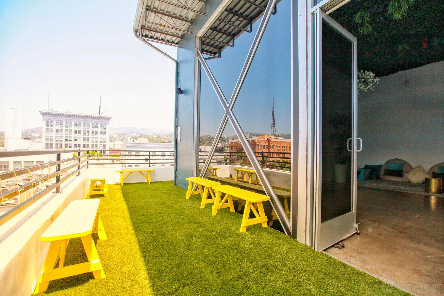 A loft terrace with artificial grass, yellow picnic tables, and a metal railing at The Secret Garden Loft.