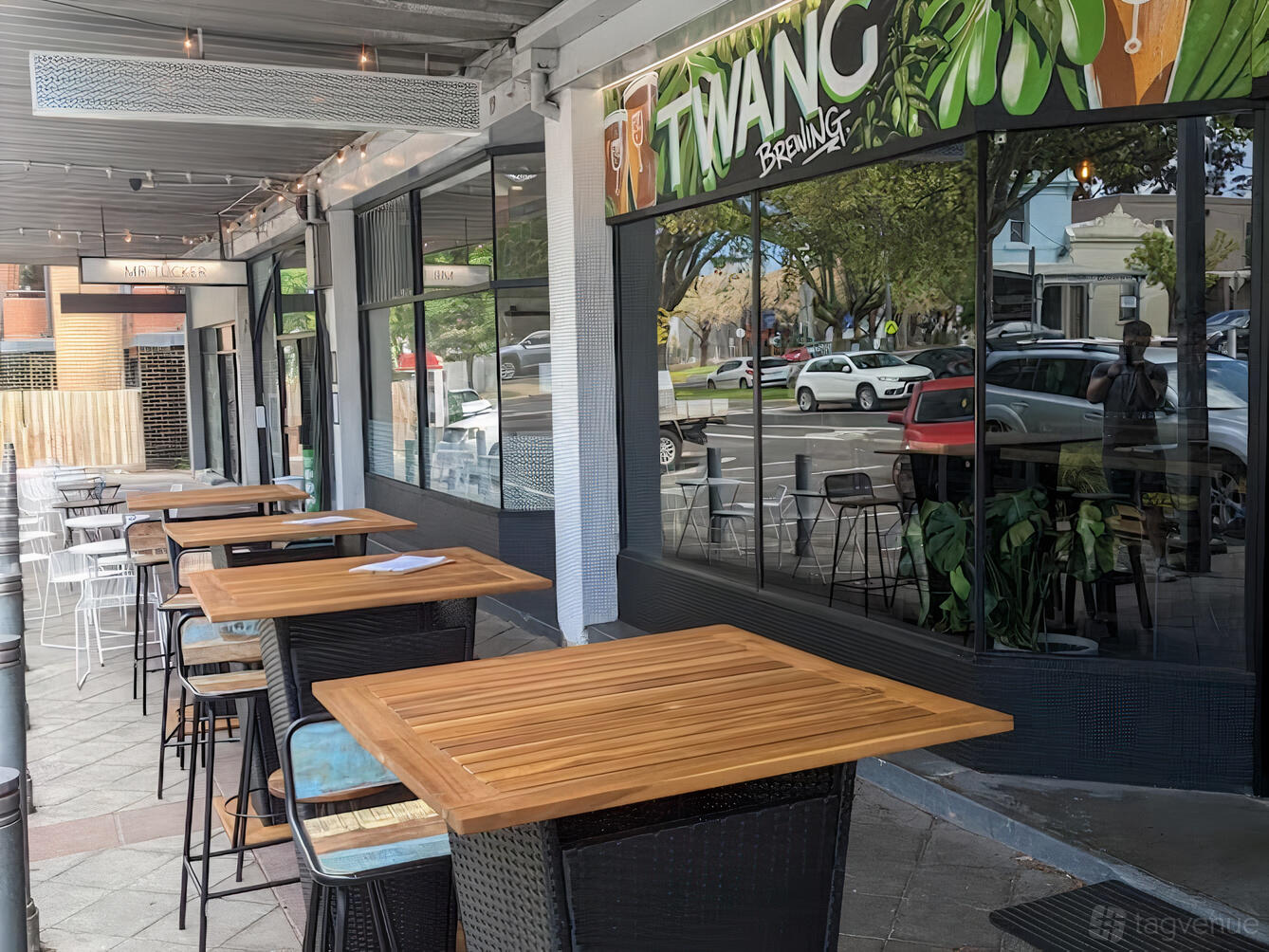 A terrace at a pub with tall wooden tables, woven stools, and large windows at Twang Brewing.