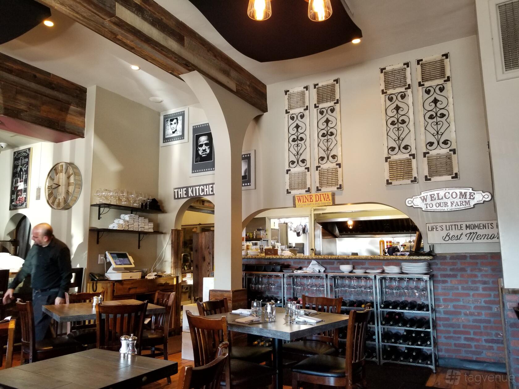 A restaurant with wooden tables, exposed beams, wall art, and open kitchen shelves at Farm and Vine.