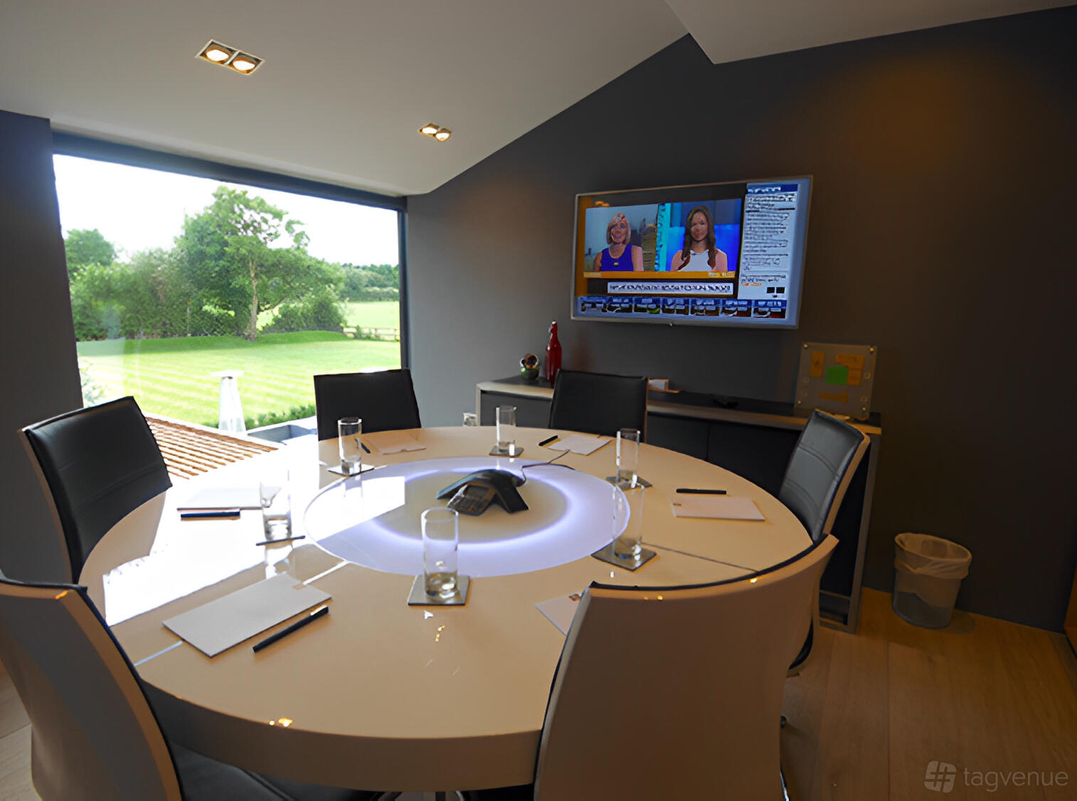 A meeting room with a round table, six leather chairs, large window, and wall-mounted TV at The Colony HQ.