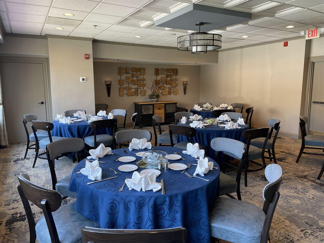 A restaurant dining room with round tables dressed in blue linens and folded napkins at Tyson's Social Tavern.