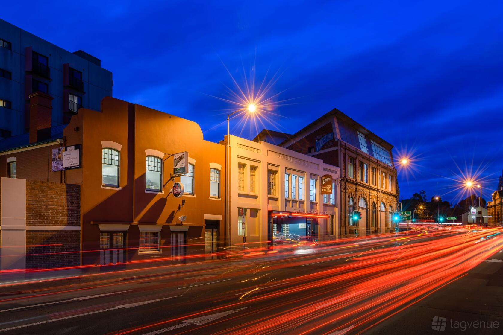 A hotel with a historic brick façade and large windows illuminated by streetlights at The Old Woolstore Apartment Hotel.
