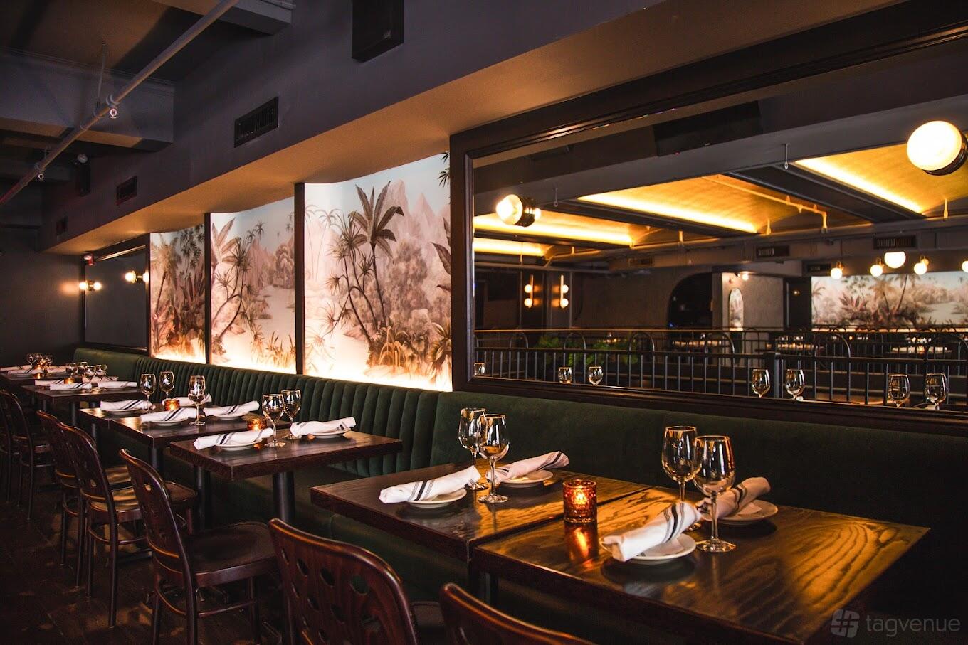 A dining room in a bar with dark wood tables, green velvet banquette seating, and wall art at 5th and Mad.