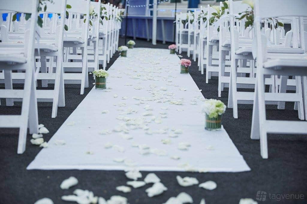 A yacht event space with white chairs in rows, floral aisle decor, and scattered petals at Yacht Events NYC.