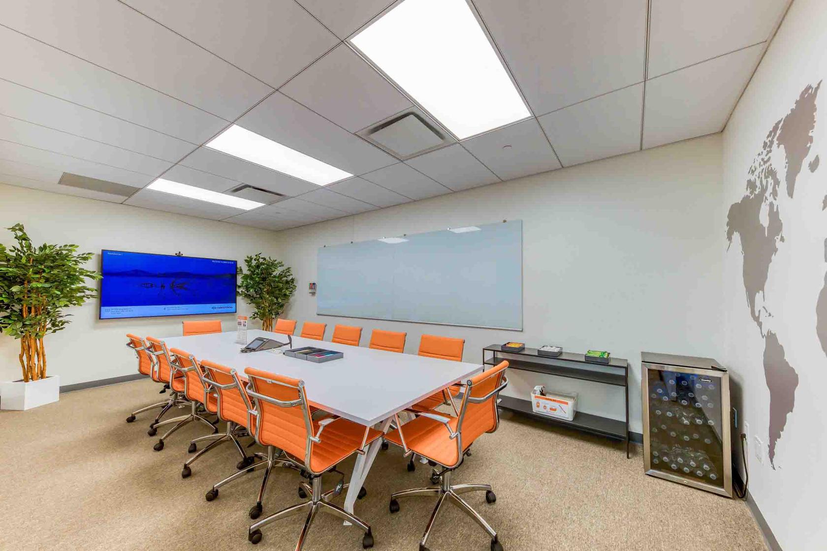 A boardroom with orange chairs, a large whiteboard, wall-mounted TV, and world map decal at WorkSocial.