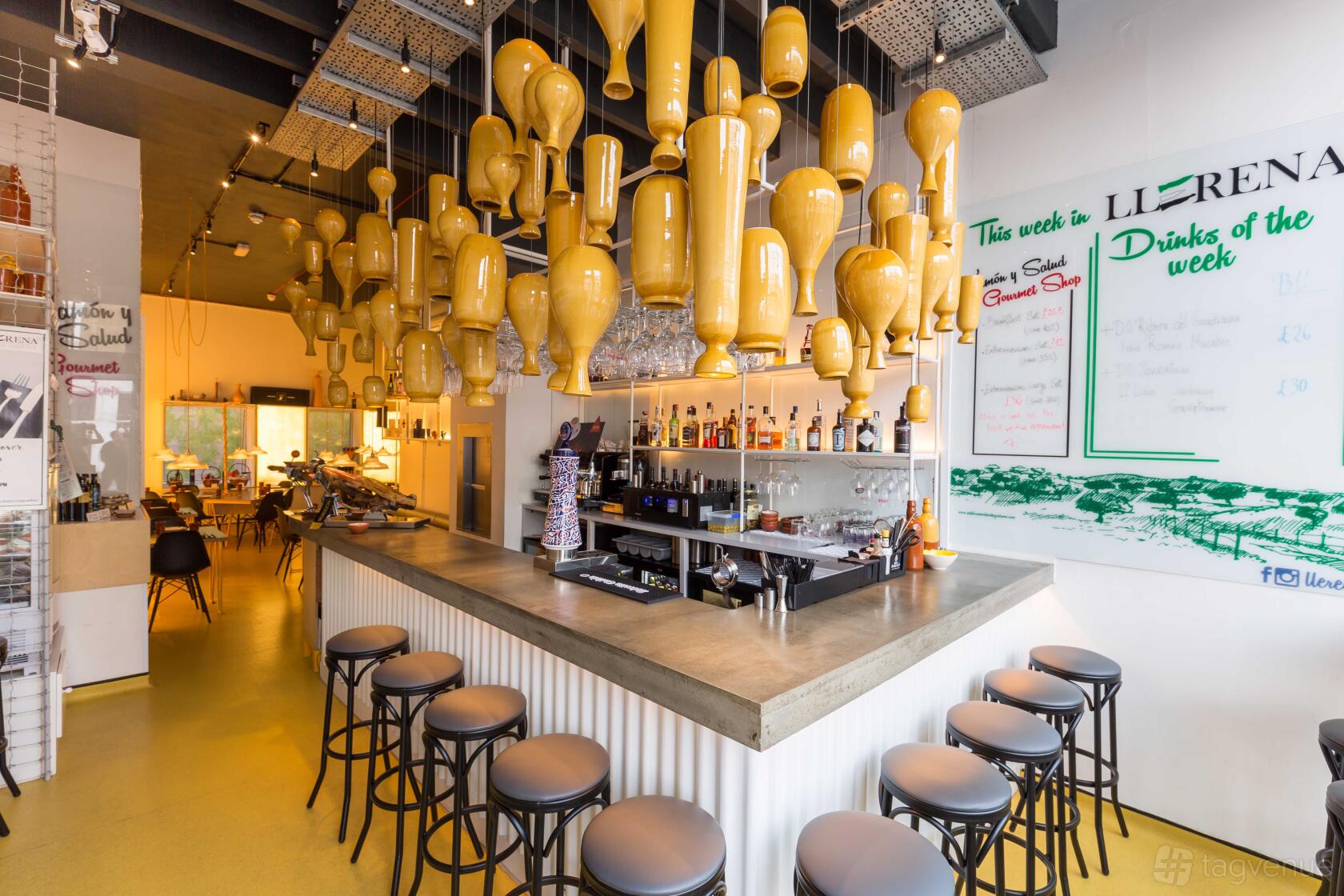 A bar with a concrete countertop, rows of bar stools, and hanging ceramic jugs above the counter at Llerena Tapas Bar.