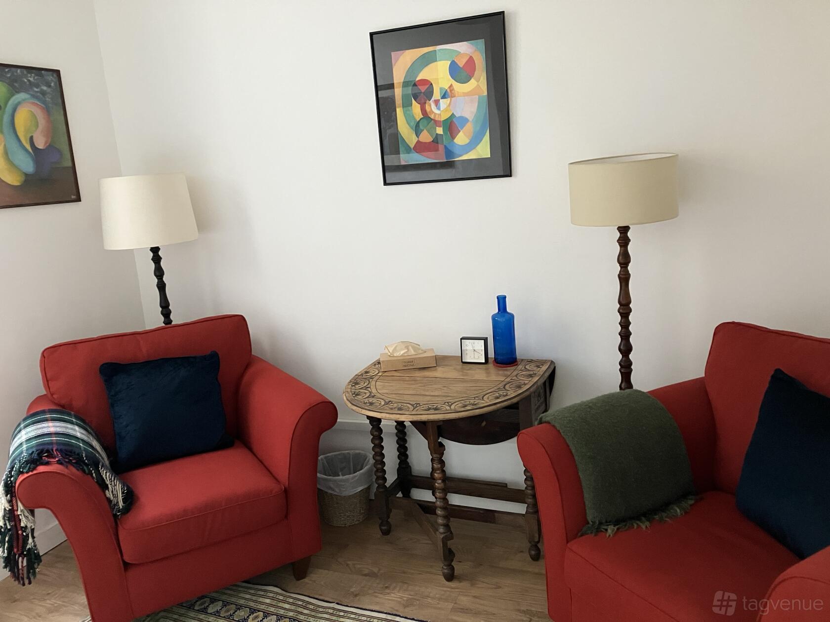 A therapy room with two red armchairs, decorative table, and colorful abstract art at Delancey Therapy Rooms.