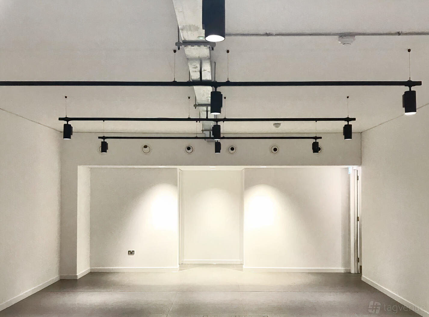 A function room with white walls, exposed ceiling pipes, and track lighting at The Old Street Gallery.