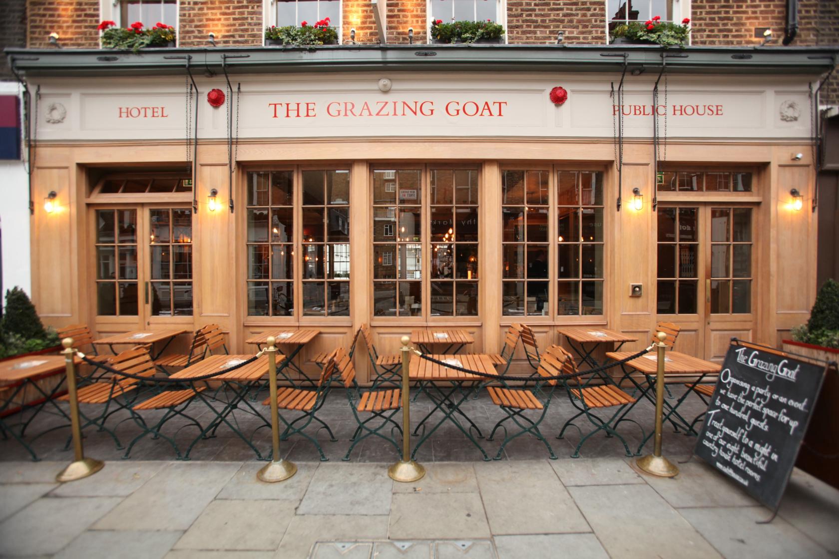 A hotel with a brick facade, large windows, and wooden outdoor seating at The Grazing Goat Marylebone.