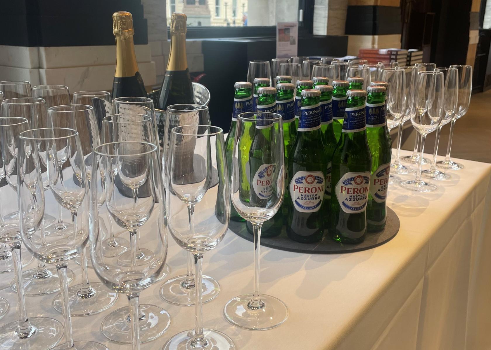 A gallery setup with wine glasses, champagne bottles, and Peroni beer on a white table at Iconic Images Gallery, Piccadilly.