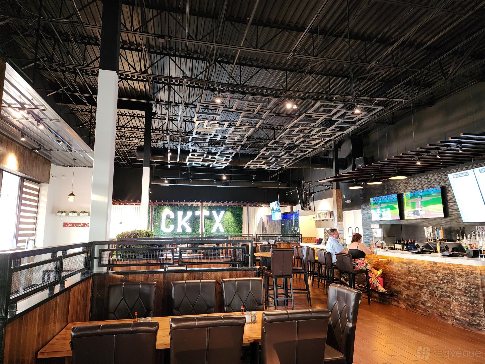 A restaurant with high ceilings, cushioned booth seating, and a bar with mounted TVs at Cutten Kitchen.