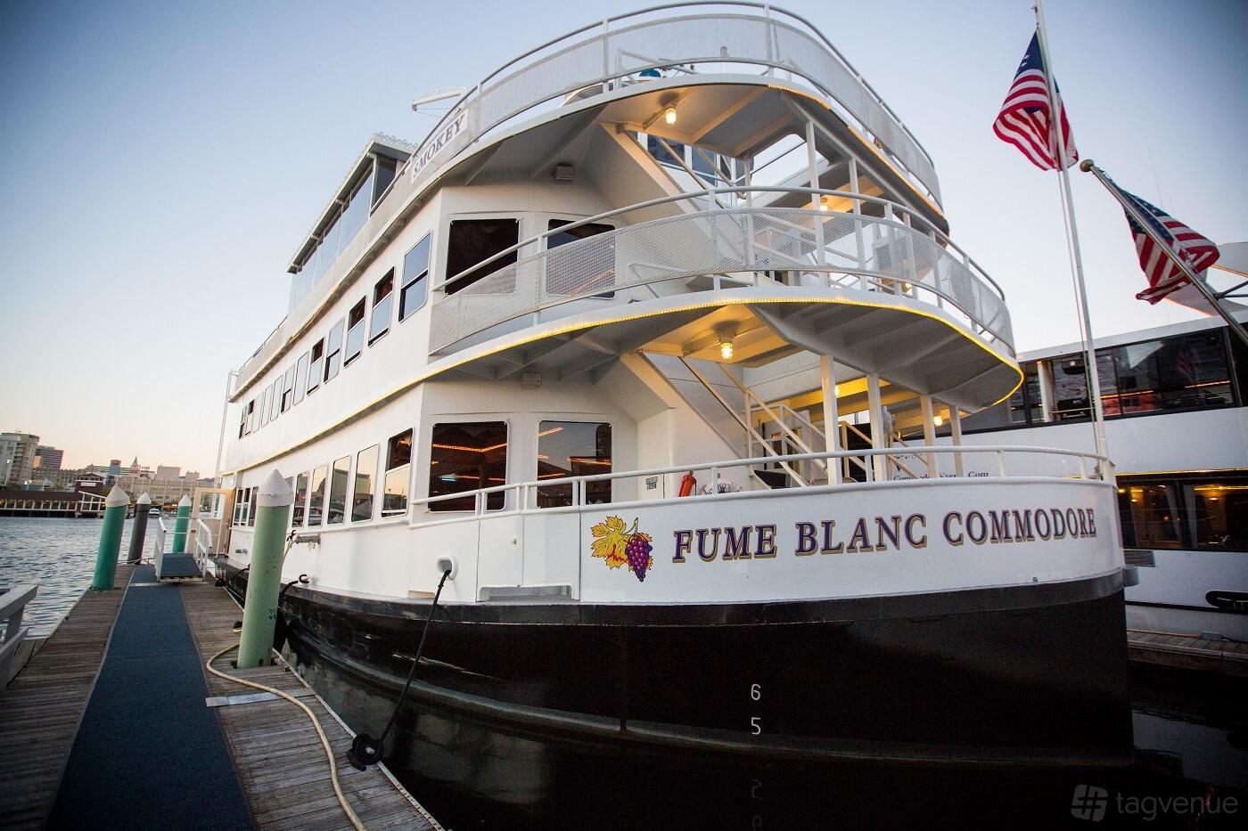A white multi-deck boat with railings and American flags docked at Fume Blanc.