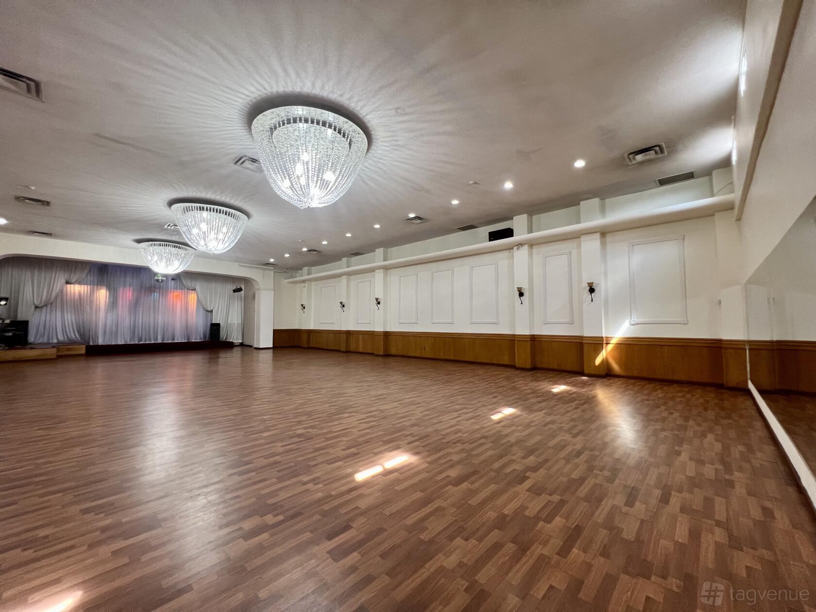 A dance studio with wood flooring, large chandeliers, wall sconces, and a curtained stage at Ballroom Expressions Dance Studio.
