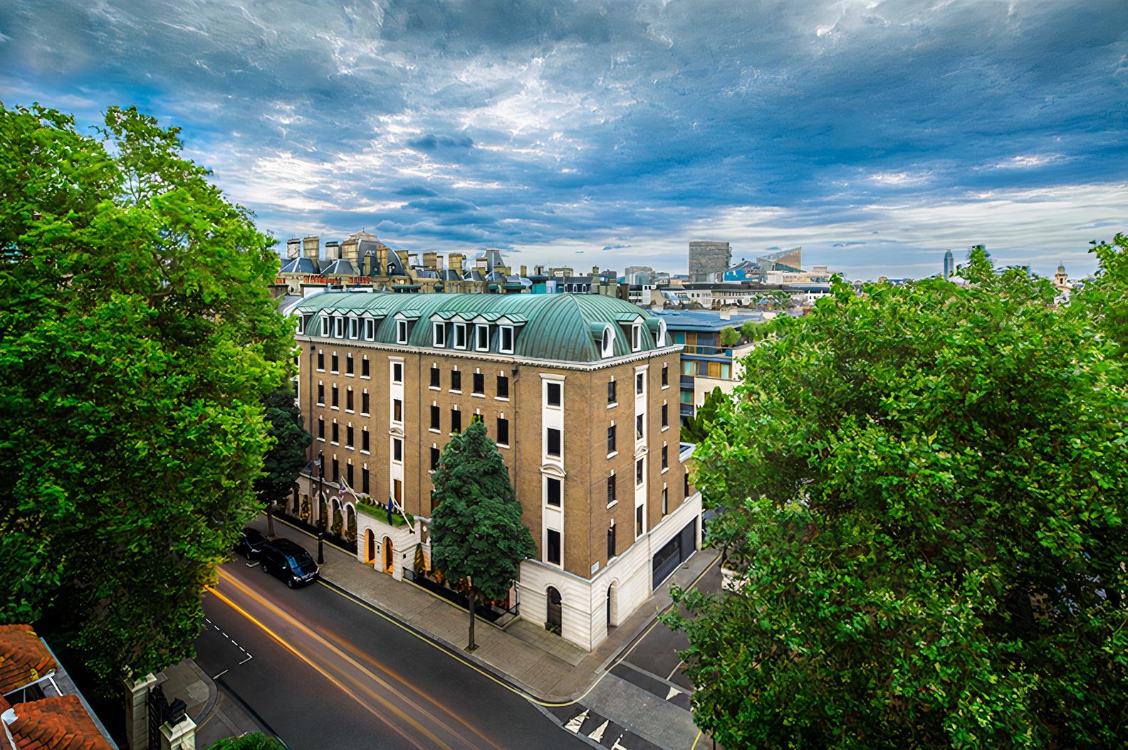 A brick restaurant with a green mansard roof set among leafy trees at COMO The Halkin.