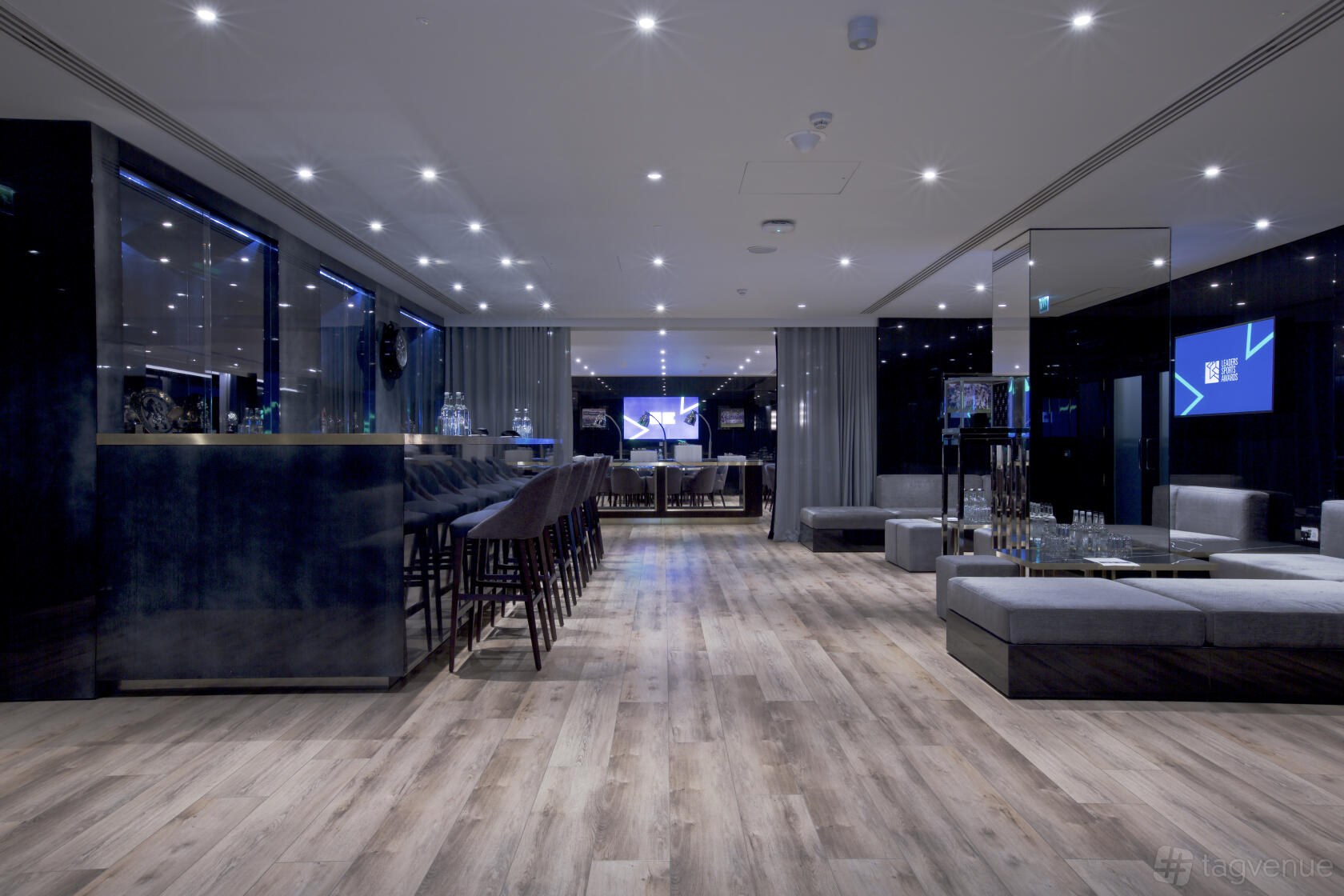 A lounge with a sleek bar, plush gray sofas, and wood flooring at Chelsea Football Club.