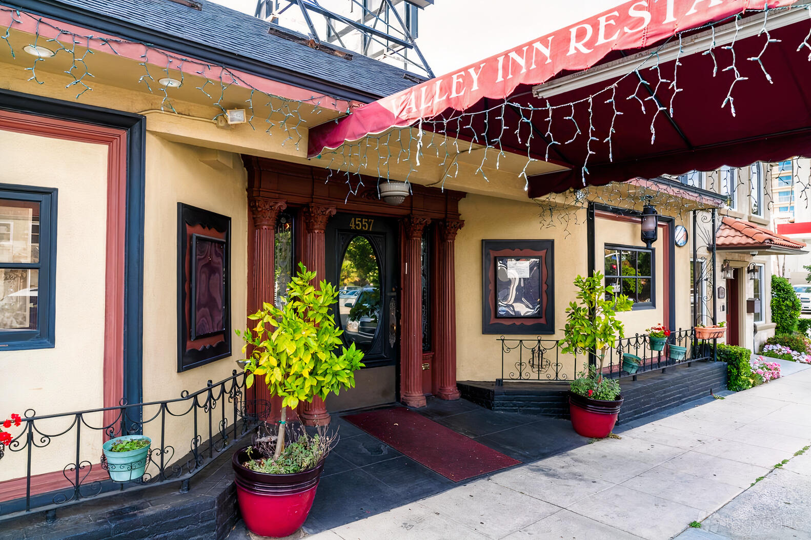 A restaurant entrance with a red awning, potted plants, and decorative columns at Valley Inn Restaurant and Bar.