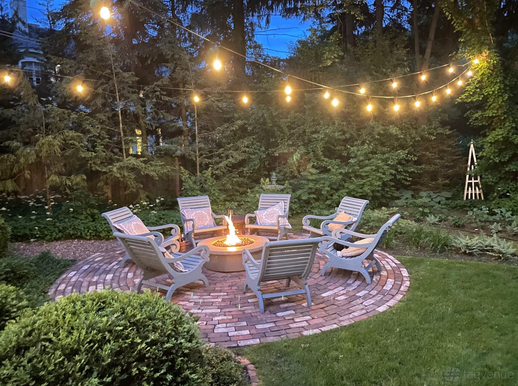 A house with a circular brick patio, fire pit, Adirondack chairs, and string lights at Grace French Manor Home & Gardens.