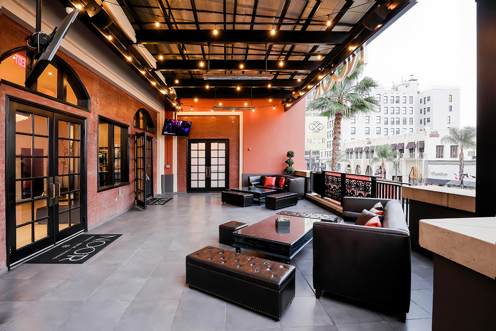 A covered terrace with string lights, lounge seating, and city views at Noor Events.