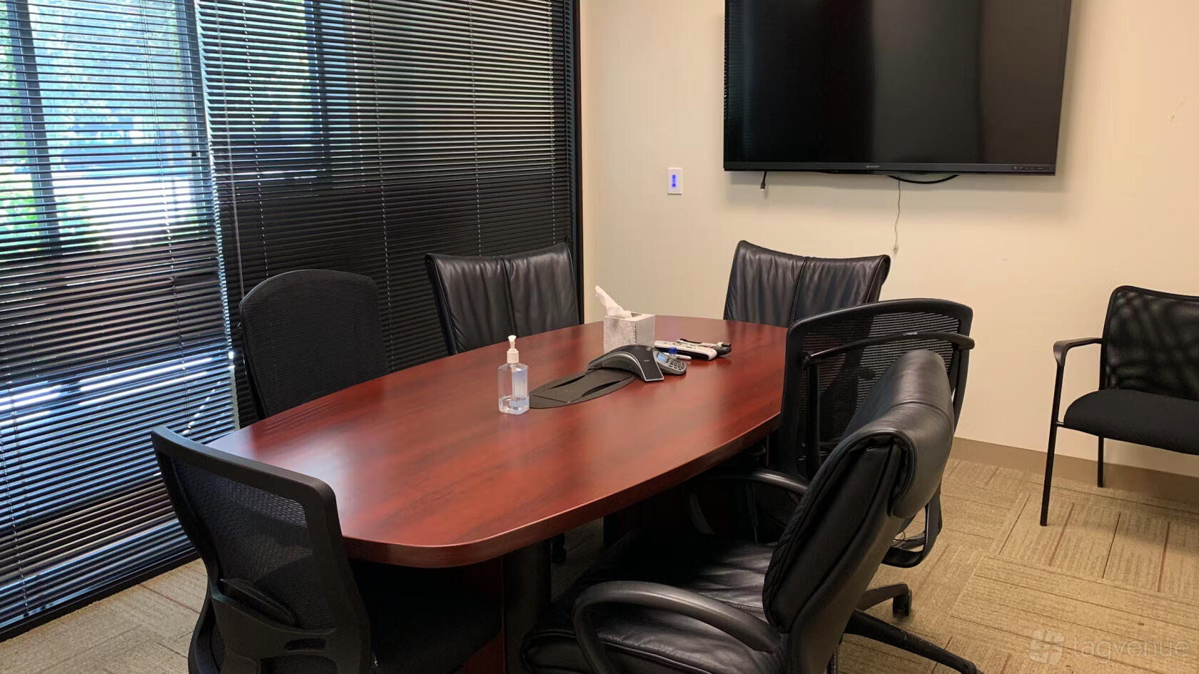 A coworking space with a wooden conference table, black leather chairs, and a wall-mounted TV at JJ Lake Business Center.