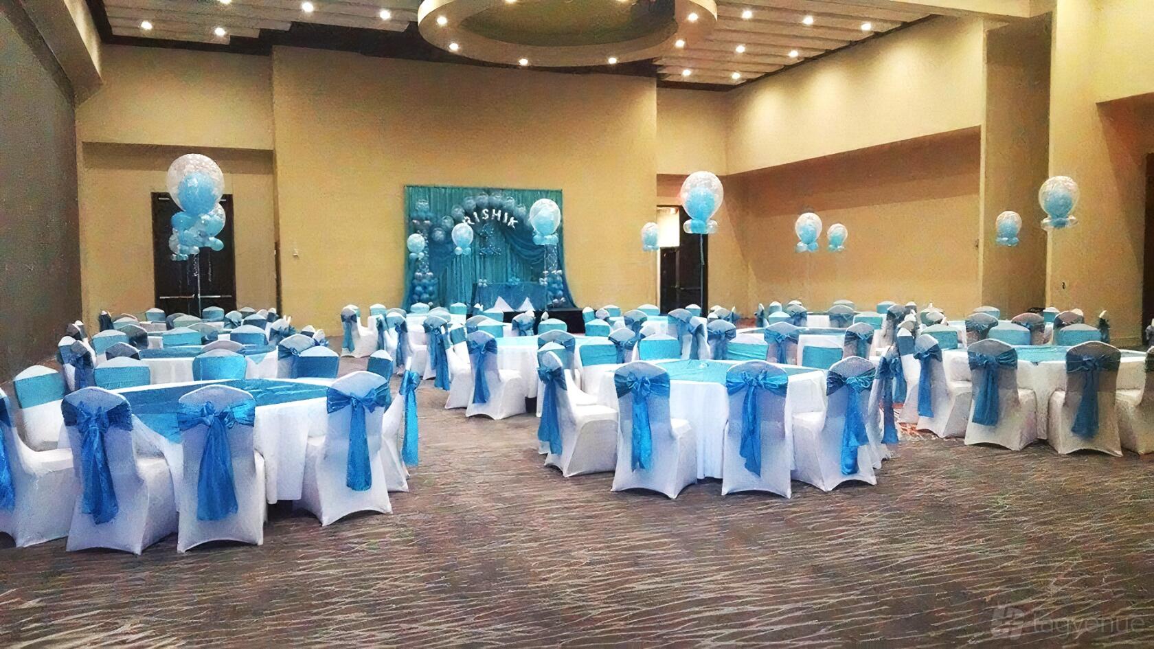 An event venue with round tables draped in blue linens and white chairs with blue sashes at SLPS Event Center.