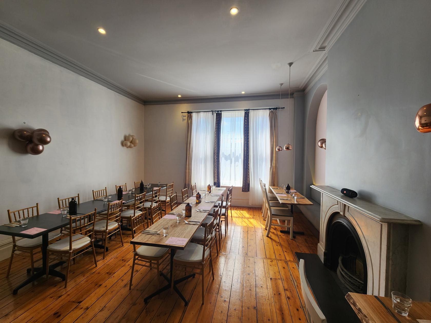A function room in a restaurant with wooden floors, natural light, and an ornate fireplace at Mokum.