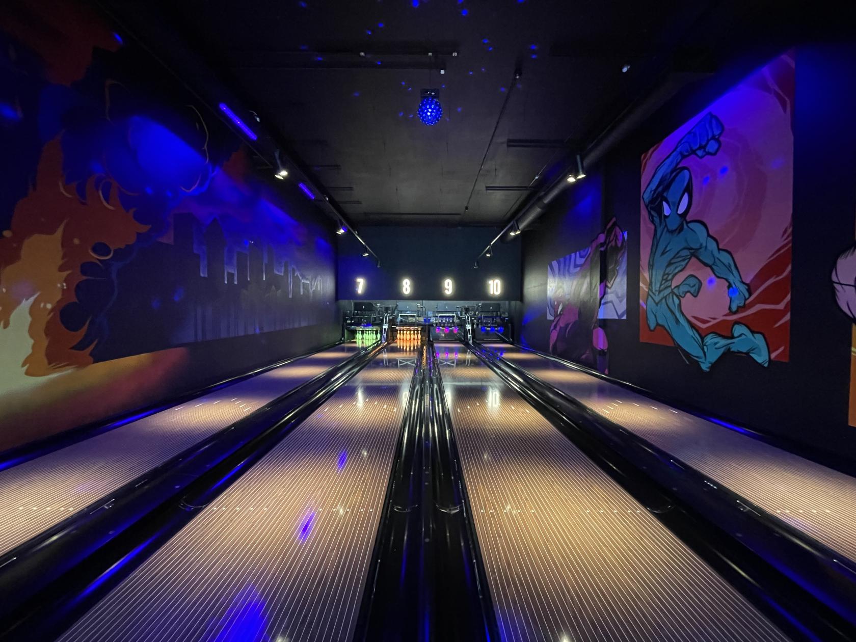 A bowling alley with illuminated lanes, colorful wall murals, and electronic scoreboards at The Light Stockport.