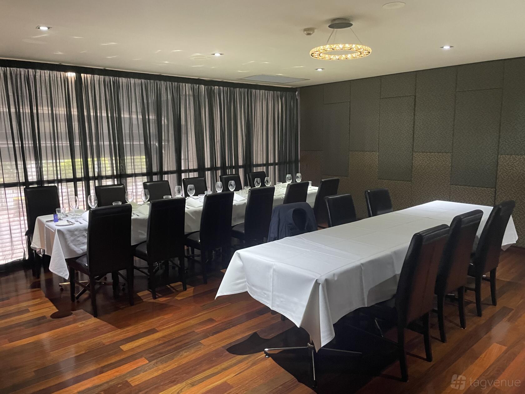 A dining room with two long tables set with white tablecloths, black chairs, and wood flooring at Escagrill.