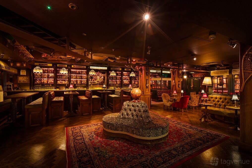 A cocktail bar with vintage armchairs, ornate rugs, and backlit shelves of spirits at Mr Fogg's Society of Exploration.