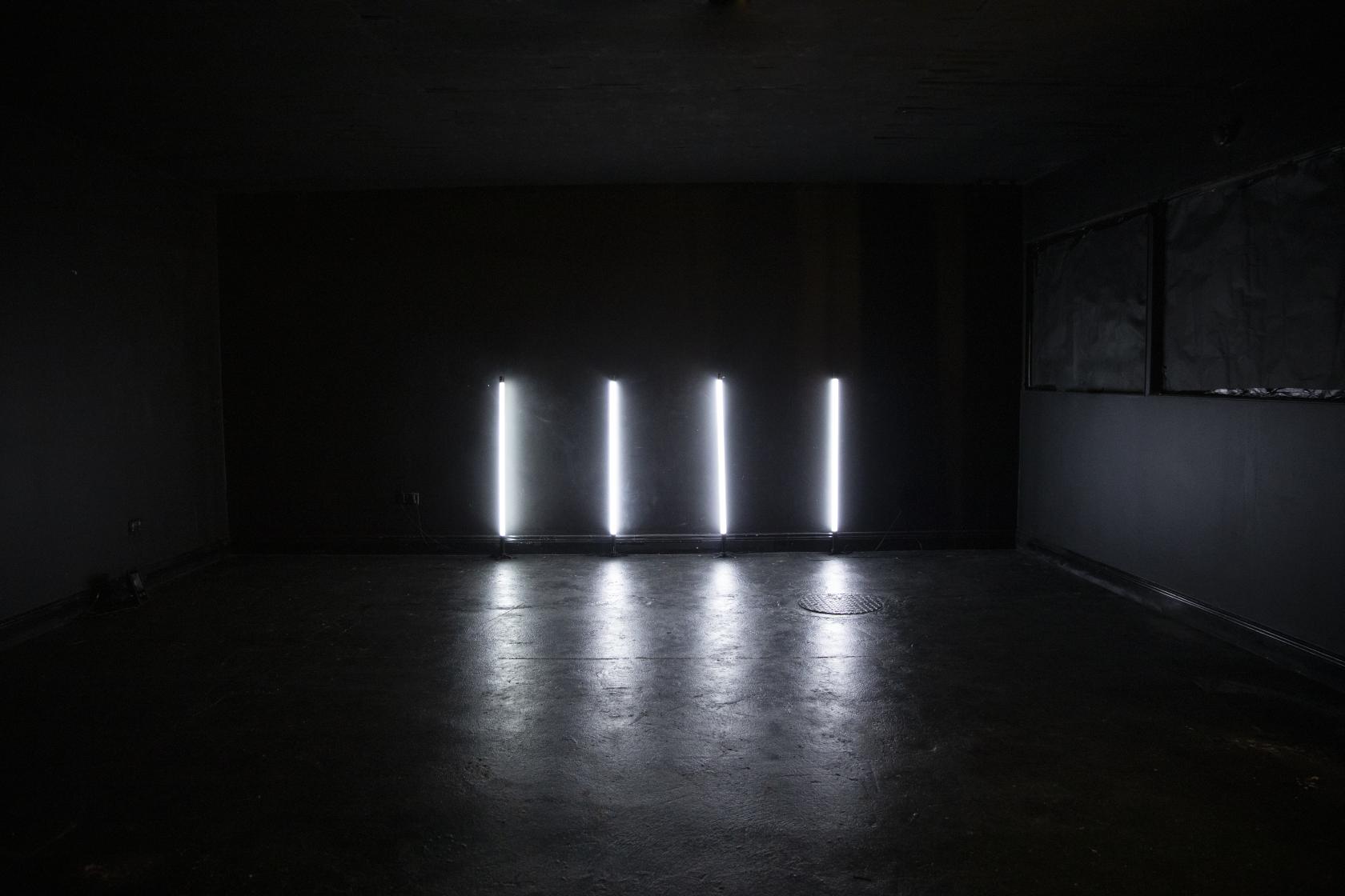 A dark photo studio with black walls and four vertical white light tubes at Blackout studio & Medical Room.