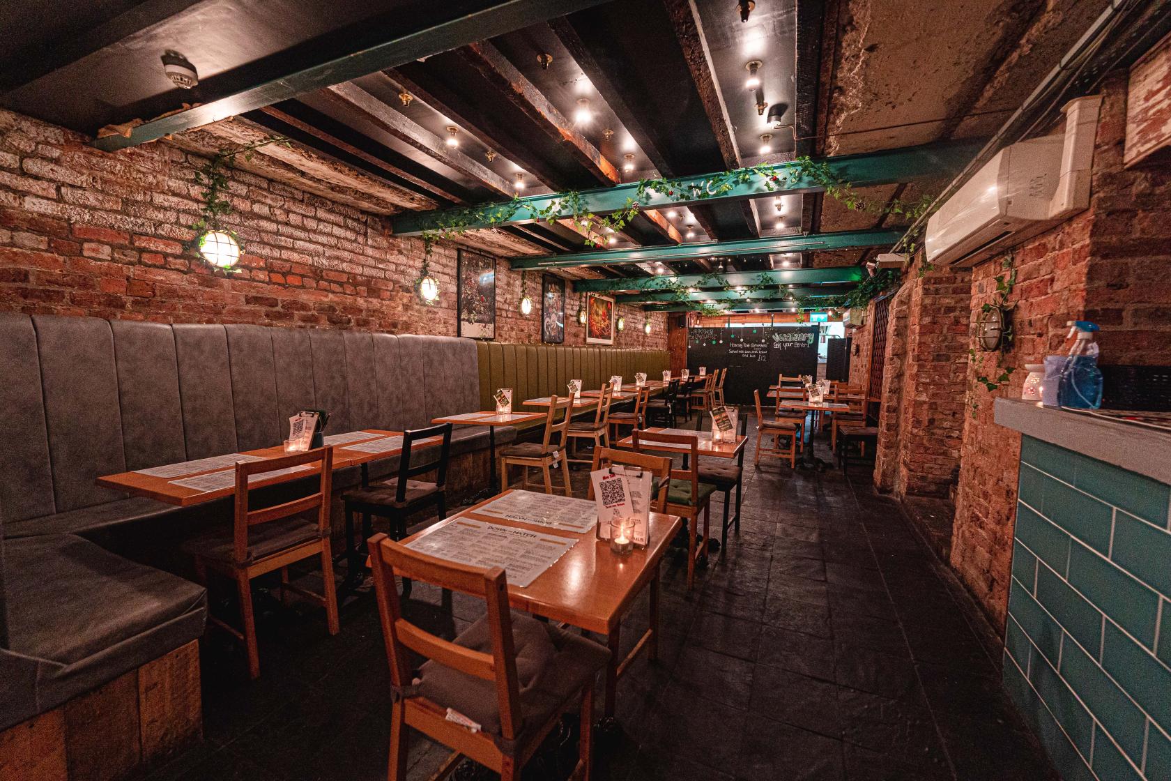 A restaurant with exposed brick walls, wooden tables, cushioned bench seating, and pendant lights at Down the Hatch.