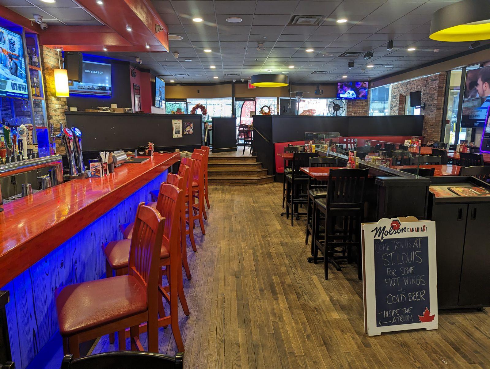 An event space in a restaurant with red bar seating, wooden floors, and a chalkboard sign at St. Louis Bar & Grill Atrium.
